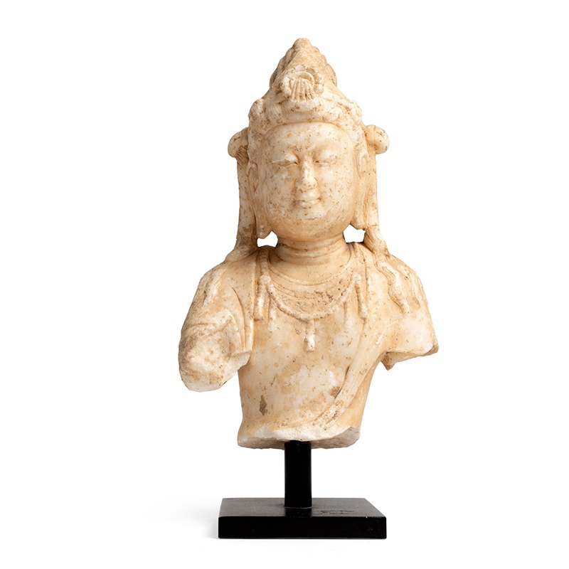 Lot 81 | TANG STYLE WHITE MARBLE TORSO OF A BODHISATTVA | 唐式白大理石雕菩薩像 the bodhisattva carved wearing a beaded and foliate necklace, his face depicted in minute details with serene expression, his head wearing a jewelled crown, mounted on a metal base (Qty: 1) 23cm high | £300 - £500 + fees
